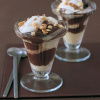 Two glass sundae dishes layered with cream and chocolate with nuts sprinkled on top and two spoons on the side