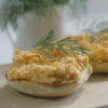 a picture of a bagel cut in half with scrambled egg and a garnish of dill on top 