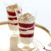 Two tall dessert glasses filled with layers of cream and raspberry sauce on a gold tray with two spoons on the side