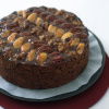 A picture of a round fruit cake decorated with nuts on the top on a dark plate