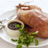 a picture of a white plate with a whole roast duck with a bowl of cherry sauce and a silver carving knife and fork