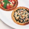 a pictue of two circular galettes, one with tomatoes goats cheese and basil and one with spinach and feta