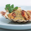 a pictur eof cooked scallops in a shell with lentils sauce and parsely garnish on the top