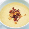 a white bowl of split pea soup garnished with crispy bacon and croutons