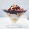 a glass sundae dish with greek yoghurt, bananas and chocolate in layers