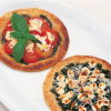 a pictue of two circular galettes, one with tomatoes goats cheese and basil and one with spinach and feta