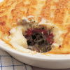A white dish of vegetarian shepherds pie with a portion removed showing the pulses and tomatoes