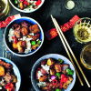 Colourful litle bowls of beef and black pepper potatoes on a black table with chopsticks resting on the side