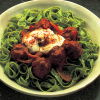 a picture of cooked Meatballs Braised in Goulash Sauce sitting on green noodles in a yellow bowl