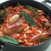 A picture of cooked cassoulet in a black casserole showing sausages, beans, bay leaves and tomatoes