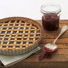 a picture of a linzertorte tarte in a flan tin with latticed pastry across the top and a jar of jam and spoon next to it