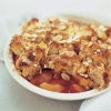 cooked plum and almond cobbler with pastry topping and flaked almonds in a white bowl