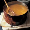 A copper saucepan full of cooked mulligatawny soup with a wooden spoon resting on the rim