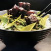 Cooked pork and stirefry greens in a brown bowl with two chopsticks resting on the side