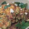A white bowl of cooked potato cakes with feta cheese and parsley scattered on top