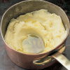 A copper pan of lovely mashed potato and cloves of garlic in a pool of olive oil