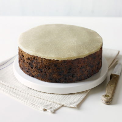 a Picture of a fruit cake on a white plate with a layer of marzipan on th top
