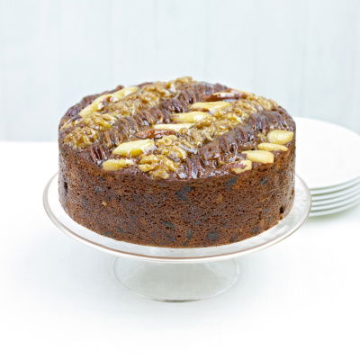 A picture of a fruit cake decorated with nuts on the top on a white cake stand