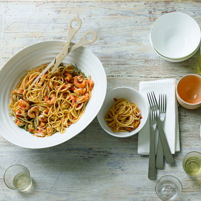 A table set with an oval dish of seafood linguines with water glasses, knives and forks,  and a green bowl of watercress salad on the side