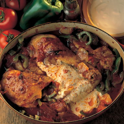 A round oven dish of cooked chicken paprika with green peppers and soured cream on the top