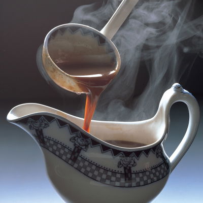 A blue and white china gravy boat with gravy being poured in from a ladle above it