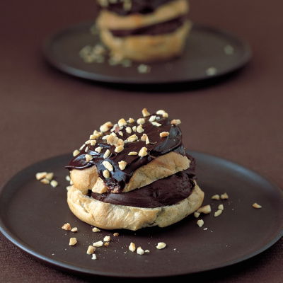 A choux bun split in half horizontally and filled and topped with a chocolate mousse mixture and coated with chocolate icing and chopped nuts.