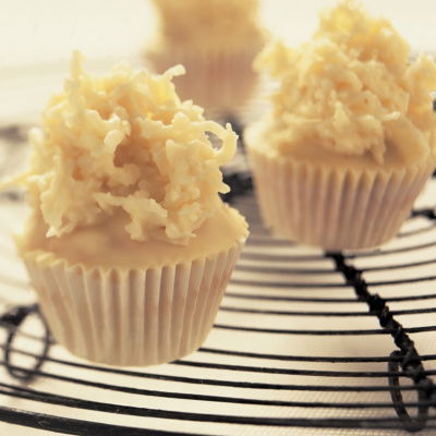 Three white chocolate muffins on a black cooling tray with shredded coconut on the top