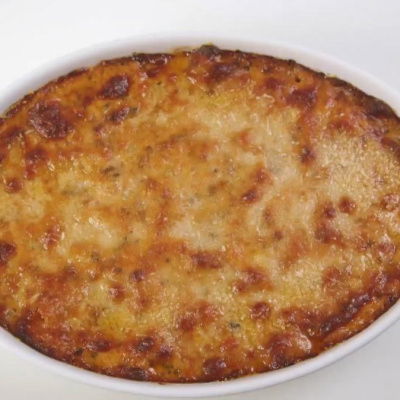 An oval white dish containing baked pasta with cheese browned on the top