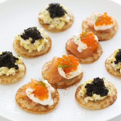 a picture of a white plate of little blinis with smoked salmon and caviar on the top