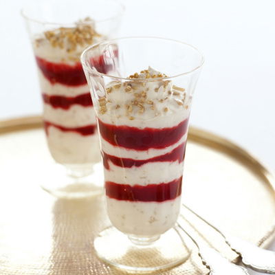 Two tall dessert glasses filled with layers of cream and raspberry sauce on a gold tray with two spoons on the side