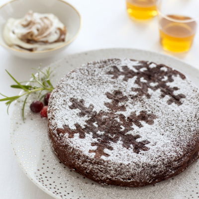 a picture of a chocolate cake with sknowflakes marked out with icing sugar, on a white plate