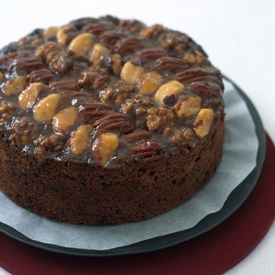 A picture of a round fruit cake decorated with nuts on the top on a dark plate