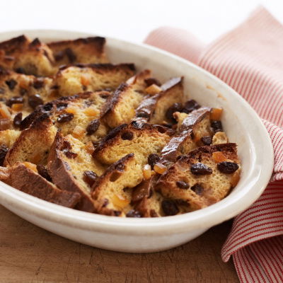 Slices of panettone bread layered in a white oval bowl with a red and white napkin next to it on a wooden board