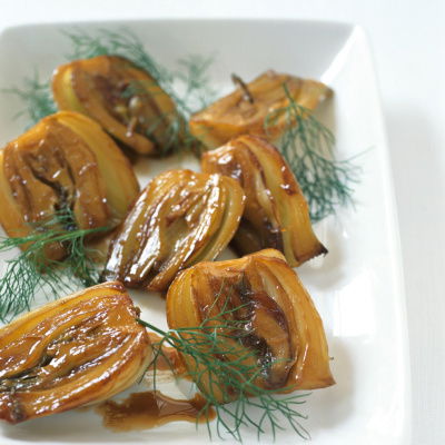 a picture of a white dish with cooked halved fennel garnished with dill