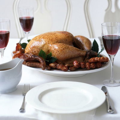a picture of a table set with white plates, cutlery wine glasses and a cooked turkey with all the trimmings