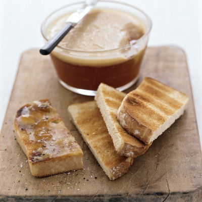 A picture of sliced toast on a wooden board with a glass container of turkey dripping and a knife resting on the edge