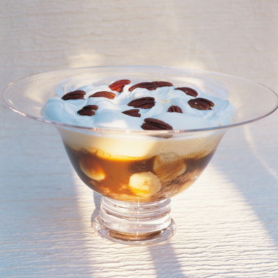a glass dessert bowl with bananas, butterscotch sauce and yoghurt layered, topped with pecan nuts