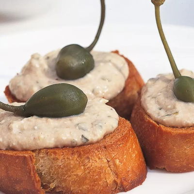 a picture of three little crostinis on a white plate with goats cheese topping and caper berries