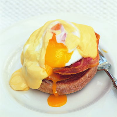 A white plate served with eggs benedict on top and a broken yolk