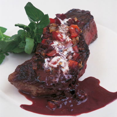 A picture of a cooked steak on. a white plate with sauce poured over the top and a watercress garnish on the side