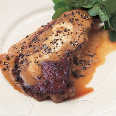 A cooked entrecote steak on a white plate covered with creme fraiche and pepper sauce and a garnish on the side