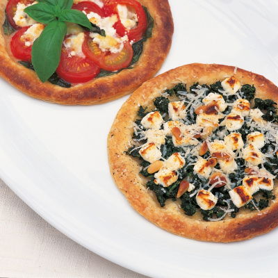 a pictue of two circular galettes, one with tomatoes goats cheese and basil and one with spinach and feta