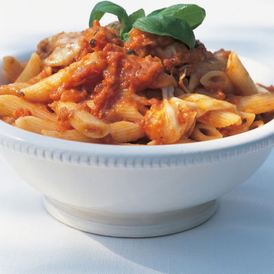 a close up of a white bowl filled with pasta and tomato sauce with basil leaves on the top