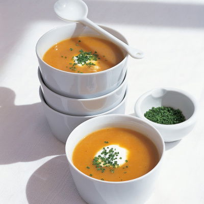 A picture of four white soup bowls with two full of root vegetable soup, a white spoon resting on the top and a bowl of chopped parsley