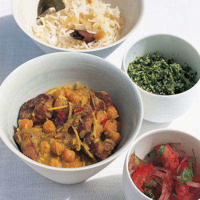 a picutre of four white dishes containing curry, rice, pickle and  sambal