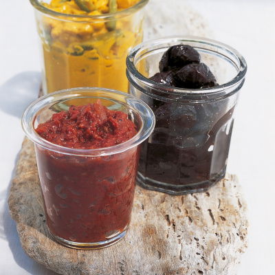 a picture of three glass jars on a wooden board with different pickles filling each one