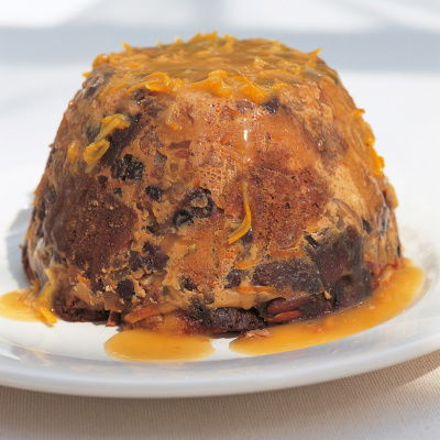 A Steamed Panettone Pudding with Eliza Acton's Hot Punch Sauce turned out on to a white plate with sauce dripping down the outside