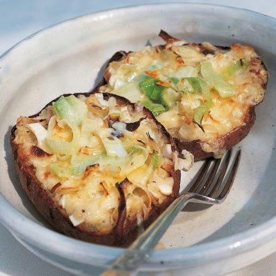 a picture of a cooked jacket potato cut in half and filled with melted cheese and leeks, resting on a plate