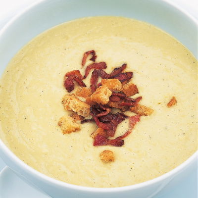 a white bowl of split pea soup garnished with crispy bacon and croutons