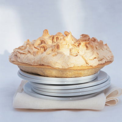 six white plates with a cooked lemon meringe pie balanced on the top